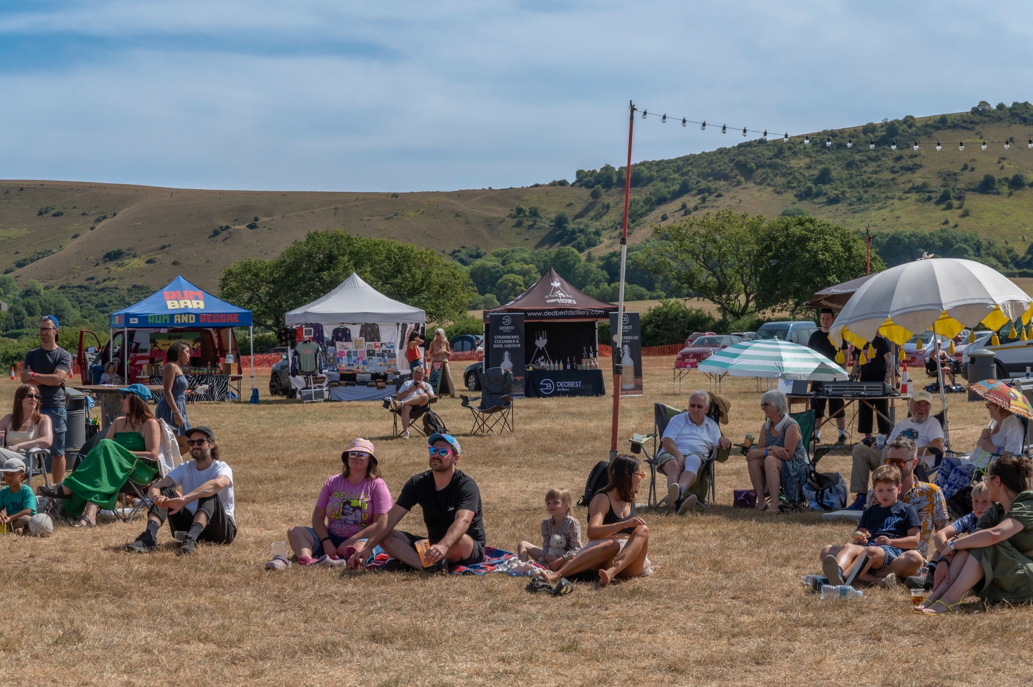 Festival visitors sitting on the grass with the South Downs behind